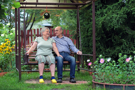 Happy elderly couple sitting on a bench in a country yardの写真素材