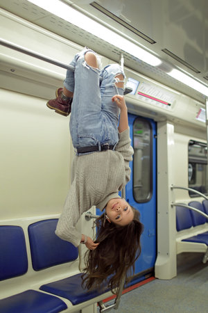 A teenage girl hangs upside down on a handrail on a subway train