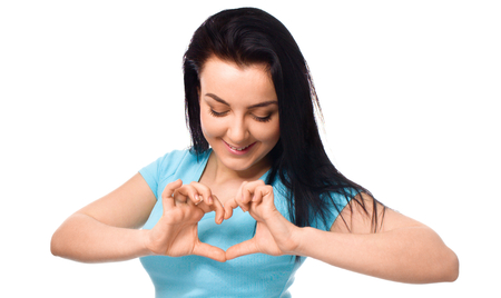 Beautiful young woman showing heart symbol gesture, isolated over white backgroundの写真素材