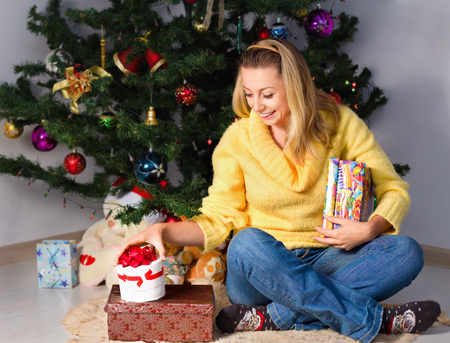Attractive young woman holding gift and sits near Christmas treeの写真素材
