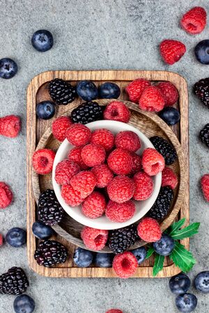 Rustic wooden plates on a concrete background, showing a mix of freshly picked berries. Raspberry, blueberry, blackberry. Flat layの写真素材