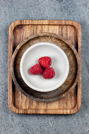 Rustic wooden plates on a concrete background, showing a mix of freshly picked berries. Raspberries,...