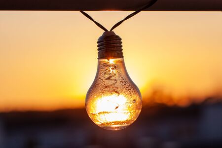 Vintage light bulbs on a the sunset background - Solar power concept. Light bulbs that are powered by photo voltaics are hanging on a balcony on a sunset backgroundの写真素材