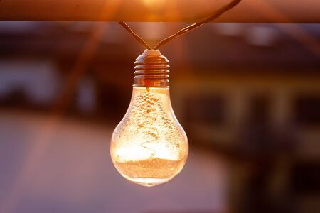 Vintage light bulbs on a the sunset background - Solar power concept. Light bulbs that are powered by photo voltaics are hanging on a balcony on a sunset backgroundの写真素材