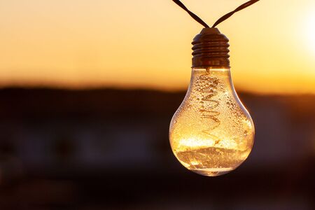 Vintage light bulbs on a the sunset background - Solar power concept. Light bulbs that are powered by photo voltaics are hanging on a balcony on a sunset backgroundの写真素材