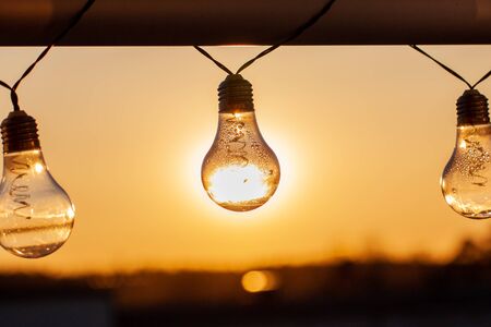 Vintage light bulbs on a the sunset background - Solar power concept. Light bulbs that are powered by photo voltaics are hanging on a balcony on a sunset backgroundの写真素材
