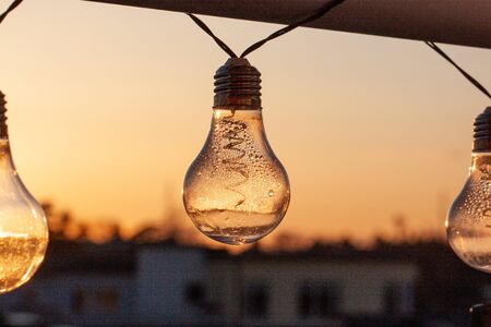 Vintage light bulbs on a the sunset background - Solar power concept. Light bulbs that are powered by photo voltaics are hanging on a balcony on a sunset backgroundの写真素材