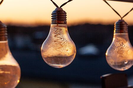 Vintage light bulbs on a the sunset background - Solar power concept. Light bulbs that are powered by photo voltaics are hanging on a balcony on a sunset backgroundの写真素材