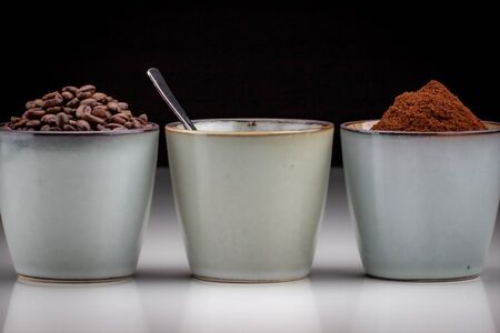 3 rustic coffee cups with coffee grounds,table coffee, and ground coffee. Standing on a white reflective table fading into a black backgroundの写真素材