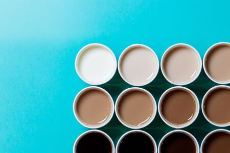 Minimalistic coffee cups arranged as to create a color gradient, with different amounts of milk added to the coffee. Turquoise background, flat lay top viewの写真素材