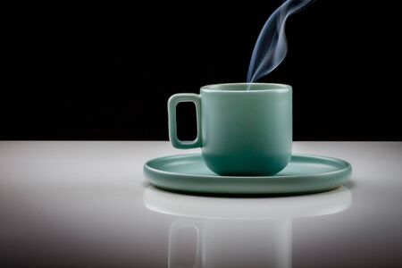 Pastel green colored coffee or tea cup with hot liquid, smoke and steam, black background. Cup standing on a slightly reflective table that fades into a black backgroundの写真素材