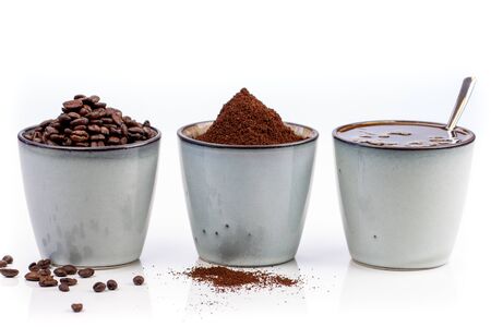 3 rustic coffee cups filled with hot coffee, beans, and ground coffee. Cups standing on a slightly reflective table that fades into a white backgroundの写真素材