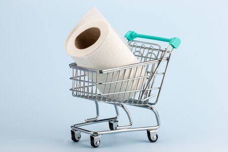 Toilet paper roll in a miniature shopping cart on a blue background.Concept of hoarding and panic buying toilet paper during the Covid-19 pandemic.の写真素材