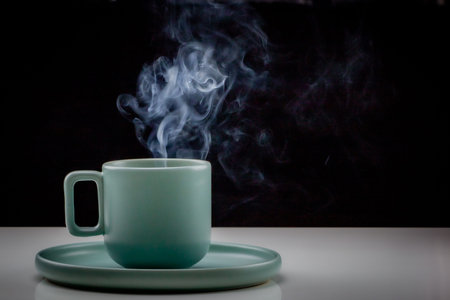 Pastel green colored coffee or tea cup with hot liquid, smoke and steam, black background. Cup...