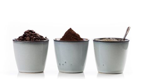 3 rustic coffee cups filled with hot coffee, beans, and ground coffee. Cups standing on a slightly reflective table that fades into a white backgroundの写真素材