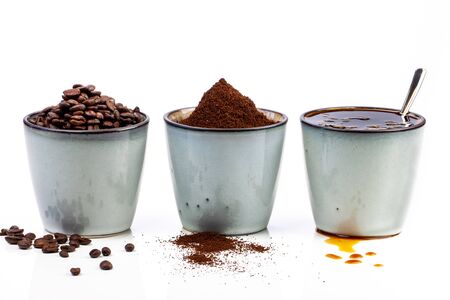 3 rustic coffee cups filled with hot coffee, beans, and ground coffee. Cups standing on a slightly reflective table that fades into a white backgroundの写真素材
