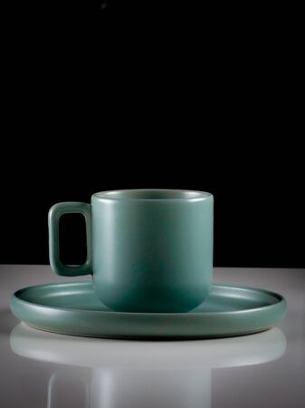 Pastel green colored coffee or tea cup with hot liquid, smoke and steam, black background. Cup standing on a slightly reflective table that fades into a black backgroundの写真素材