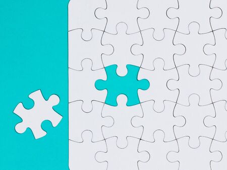 Close-up white jigsaw puzzle with a missing piece - blue backgroundの写真素材