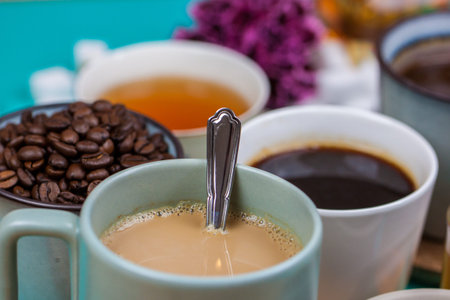 Collection of tea and coffee cups, with sugar cubes and coffee beans, on a pastel blue background....