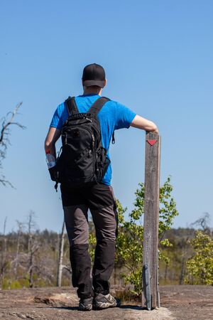 Close-up of a hiker resting his arm on a wooden pole with a red trail marker onの写真素材
