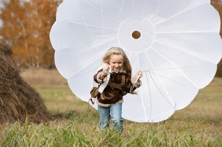 Little girl running with a parachute on the field in sunny autumn dayの写真素材