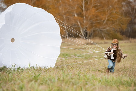 Little girl running with a parachute on the field in sunny autumn dayの写真素材