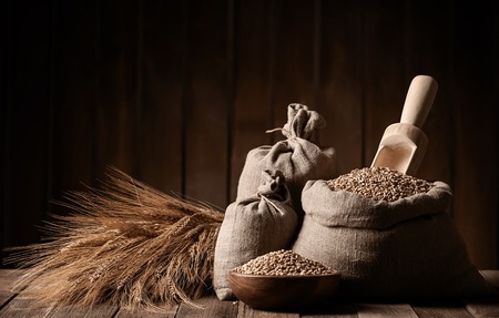 Grains of wheat in bags and ears on a wooden platformの写真素材