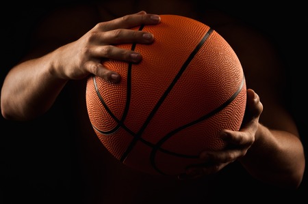 Basketball in the hands of the man close up on a black backgroundの写真素材