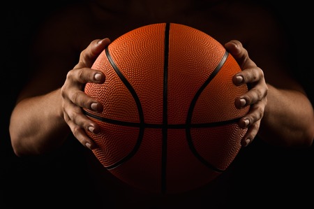 Basketball in the hands of the man close up on a black backgroundの写真素材