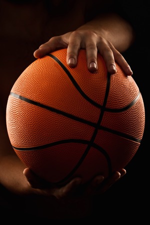 Basketball in the hands of the man close up on a black backgroundの写真素材