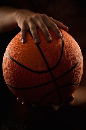 Basketball in the hands of the man close up on a black backgroundの写真素材