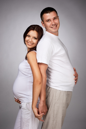 Happy pregnant woman with the husband in studio on greyの写真素材
