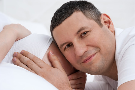Portrait of the young pair expecting the child  in bed on whiteの写真素材