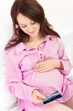 Portrait of the young pregnant girl in bed on whiteの写真素材