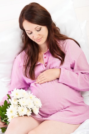 Portrait of the young pregnant girl in bed on whiteの写真素材