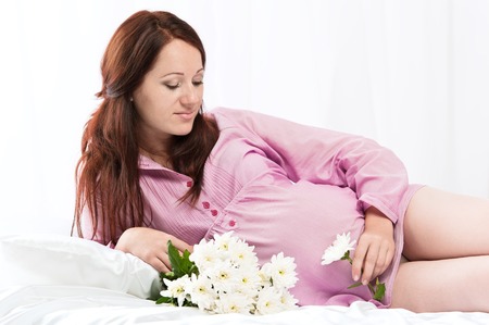 Portrait of the young pregnant girl in bed on whiteの写真素材