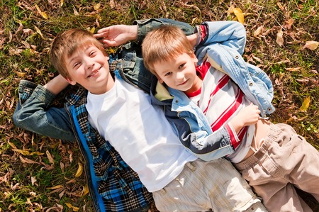 Portraits of the boys lying on the grass with autumn leaves on a warm sunny dayの写真素材