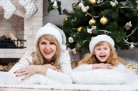 Happy mother with her daughter by the fireplace under the Christmas treeの写真素材