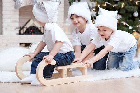 Two older brothers on the eve of Christmas rolled his younger brother on a sled through the roomの写真素材