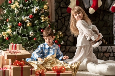 Two small children dismantle gifts under the tree in the morningの写真素材