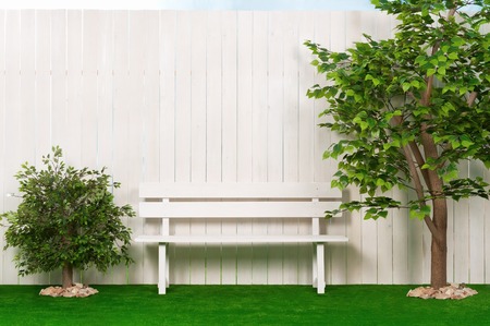 Bench by the fence with a tree and shrubs in the summer, sunny dayの写真素材