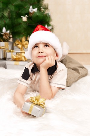 Little boy with a gift under the Christmas tree is dreamingの写真素材