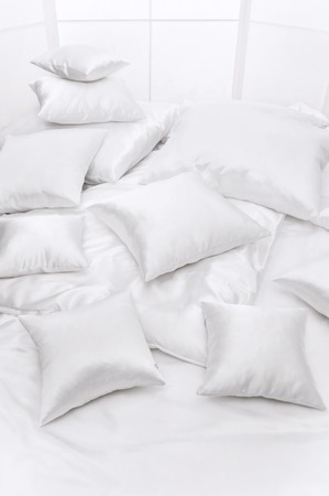 Heap of different white pillows on a bed at a windowの写真素材