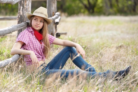 Young the girl - cowboy at an old fence in a summer sunny dayの写真素材