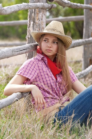 Young the girl - cowboy at an old fence in a summer sunny dayの写真素材