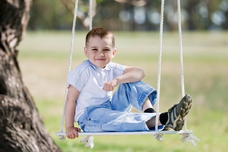 Little boy shake on a swing, adhered to the big tree, in a summer sunny dayの写真素材