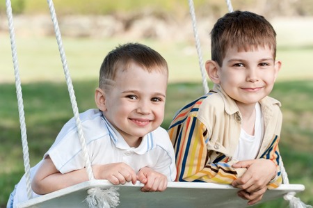 Little boys shake on a swing, adhered to the big tree, in a summer sunny dayの写真素材