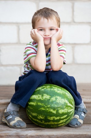 little boy with a big watermelon on the porch on a summer dayの写真素材