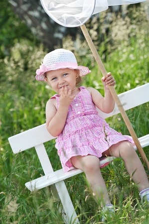 Little girl with butterfly net on the bench in sunny summer dayの写真素材