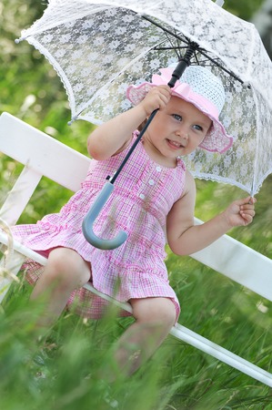 Little girl with an umbrella on a bench in the sunny summer dayの写真素材
